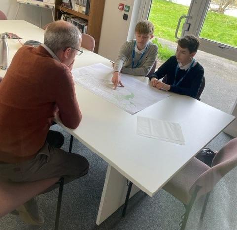 Students Alex and Matt sat opposite a staff member looking at plans and maps 