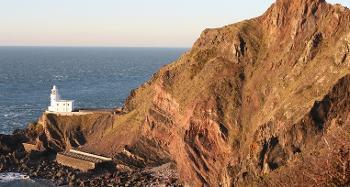 Figure 2.18: A photograph of a lighthouse on a promontory below rocky cliffs.