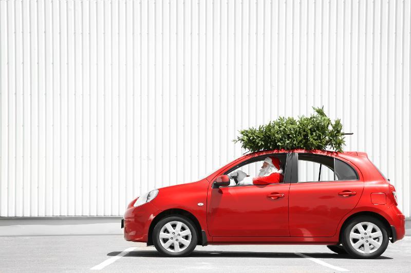 Santa driving a red car with a green christmas tree on the roof