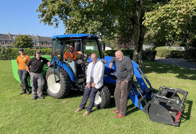 photo of a blue tractor with Councillor Bob Hicks and Councillor Chris Leather leaning against it, and Robyn, Sam and John from Torridge District Council's Grounds Maintenance Team