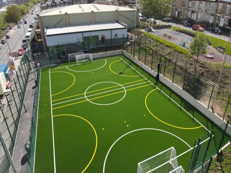 Image of a new football pitch with two goals at either end and a bright green floor with white and yellow line markings 