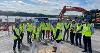 Picture of various people involved with the project, all wearing hi-vis and hard hats, breaking the ground on site