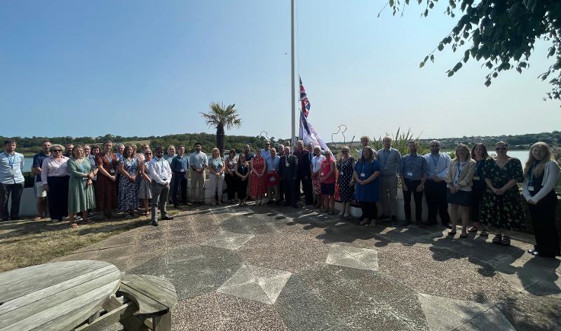 Group photo of multiple Torridge Councillors and Officers, stood at the flagpole of Riverbnak House to commemorate VJ Day