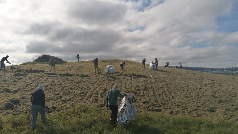 A photo of a group of people raking and bagging grass etc into bags as part of wildflower meadow management